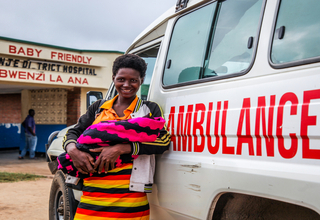 A mother with her new born baby stands with an ambulance that ferried her to the hospital ©UNFPA/ Eldson Chagara