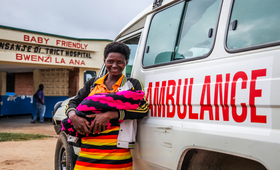 A mother with her new born baby stands with an ambulance that ferried her to the hospital ©UNFPA/ Eldson Chagara
