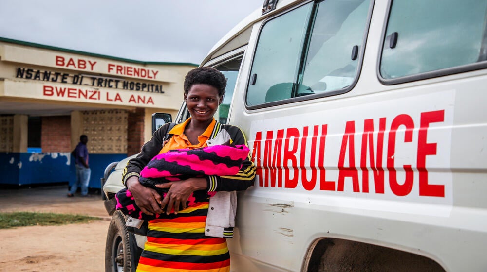A mother with her new born baby stands with an ambulance that ferried her to the hospital ©UNFPA/ Eldson Chagara